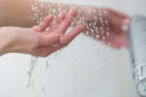 Manos bajo un chorro de agua fría, sintiendo el frescor al ducharse con agua fría.